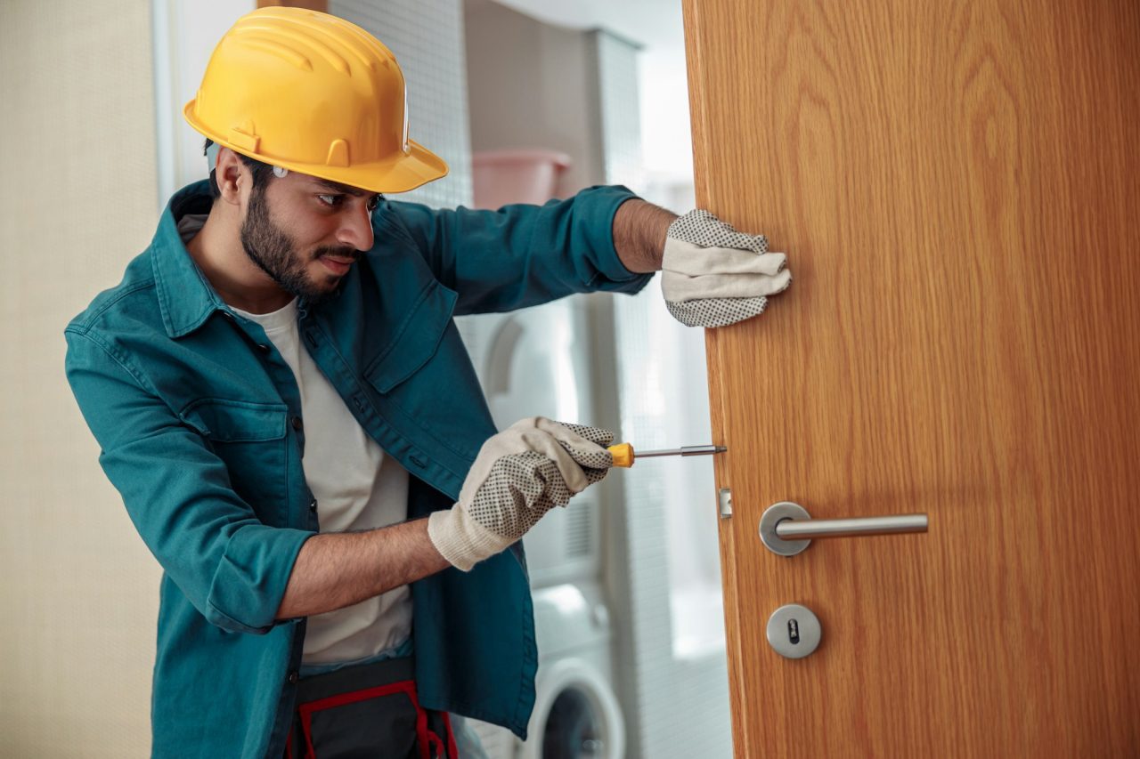 locksmith workman in uniform installing door knob professional repair service